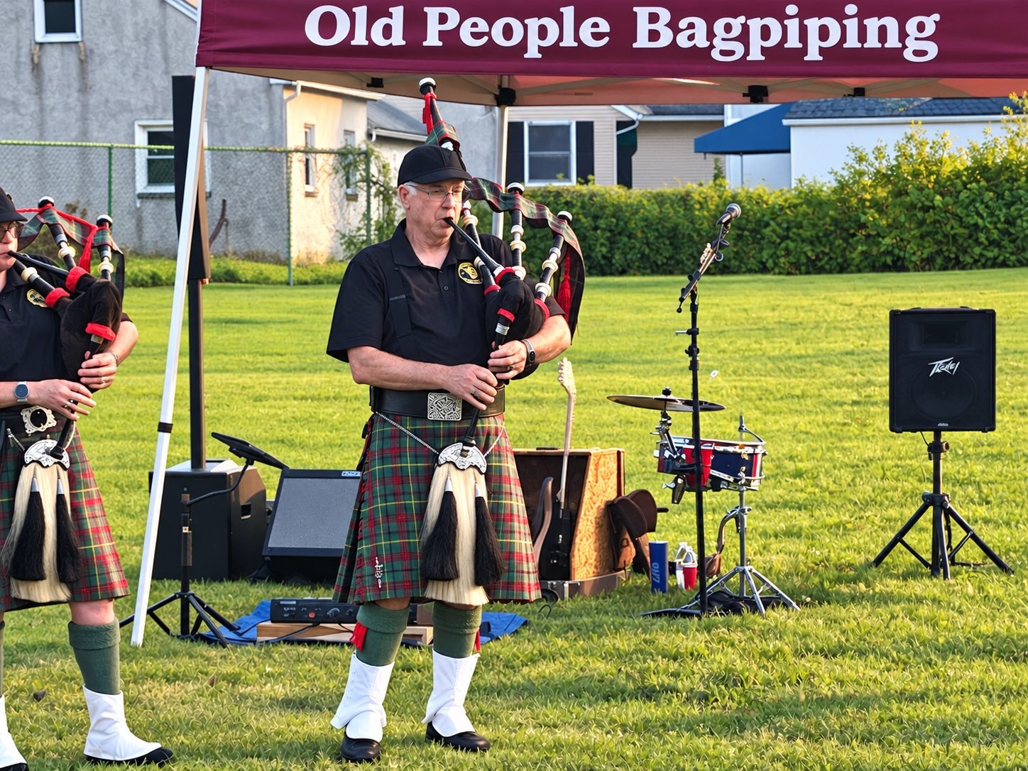 A piper in a green and red tartan kilt playing the Great Highland bagpipes on a lawn, with a second piper beside him and a canopy overhead lettered Old People Bagpiping